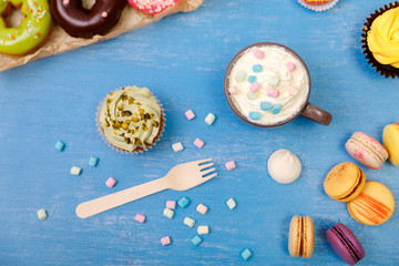 Fototapeta na wymiar Cupcakes, macaroons and donuts. Mug with whipped cream and marshmallows. Almond macaron cookies. Sweet dessert.