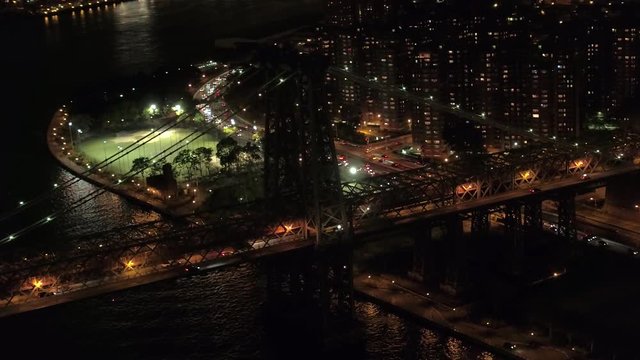 AERIAL HELI SHOT: Lit up at night historic Williamsburg Bridge leading to Manhattan residential district Little Germany neighborhood in New York City. Busy highway full of cars commuting to work