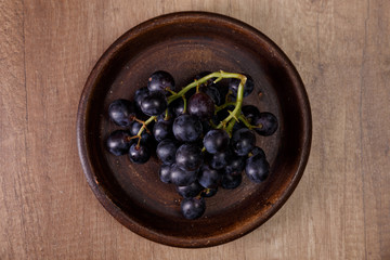 Dark grapes bunch. Ripe grape fruit on rustic plate. On wooden background.