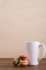 Macaroon cakes. Mockup white tea or coffee cup. Almond sweet cookies. Wooden rustic board.