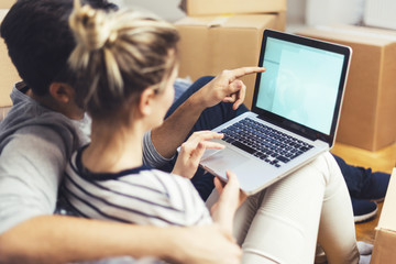 Young couple sitting between boxes and using a laptop