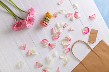 Macaroon cakes with shopping bag and Gerbera flowers. Different types of macaron. Colorful almond cookies. On white wooden rustic background.