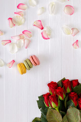Macaroon cakes with bouquet of red roses. Different types of macaron. Colorful almond cookies. White wooden rustic background.