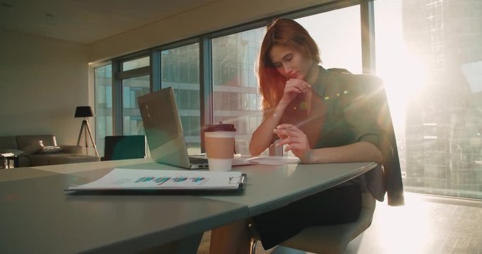 Young business woman sitting at a desk in a modern office in a skyscraper works, sun glare, steadicam shot