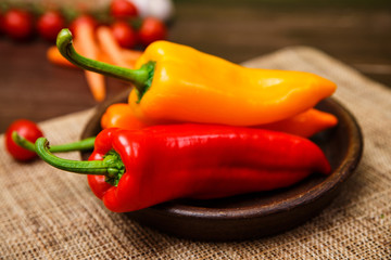 Sweet Peppers. Red, yellow and orange vegetables. Fresh natural food in rustic bowl. Organic products on wooden table with sackcloth.