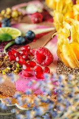 Fototapeta na wymiar Raw vegan cakes with fruit and seeds, decorated with flower, product photography for patisserie. colourful pieces of raw dessert