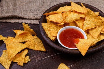 Nachos chips. Delicious salty tortilla with sweet salsa or chilli sauce on wooden background. Snack on rustic plate.