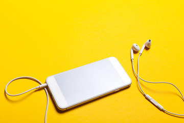 Obraz premium Close-up of smart phone with headphones on a yellow background. (Top view). Listen to music