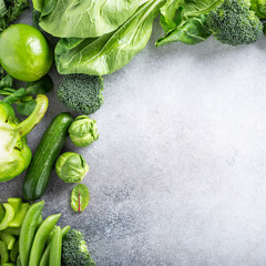 Background with assorted green vegetables, salad, broccoli, cucumber, peas and Brussels sprouts on light gray stone table top. Healthy food concept with copy space.