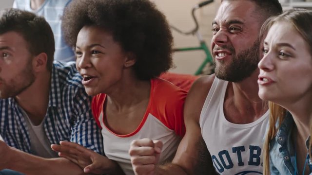 Closeup shot of group of African and Caucasian friends watching match on TV at home, yelling and celebrating victory of favorite team