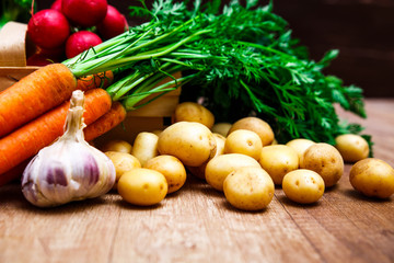 Vegetables. Potatoes, carrot and brocoli. Red radish and garlic. Wooden basket on rustic table.