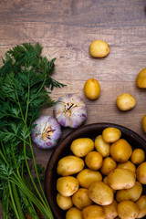 Potatoes in plate. Carrot tops, garlic and raw new potato. Fresh natural vegetables. Organic bio food on rustic wooden table.