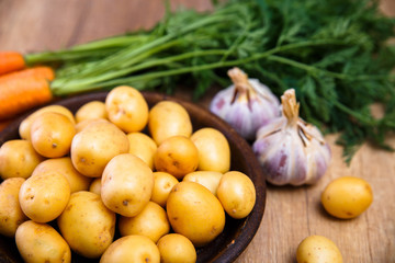 Potatoes in plate. Carrot, garlic and raw new potato. Fresh natural vegetables. Organic bio food on rustic wooden table.