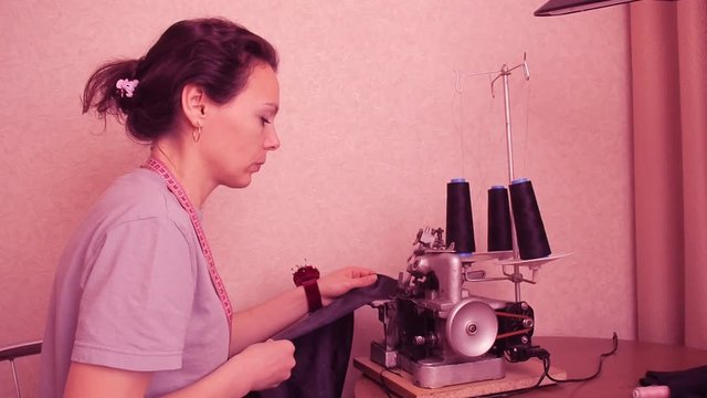 Seamstress work on the overlock. Overcast fabric. A woman in a gray T-shirt.