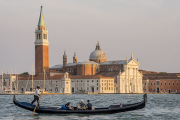 Gondola with a group of tourists on board navigates the Grand Canal with the island of San Giorgio Maggiore in the background under a beautiful light, Venice, Italy