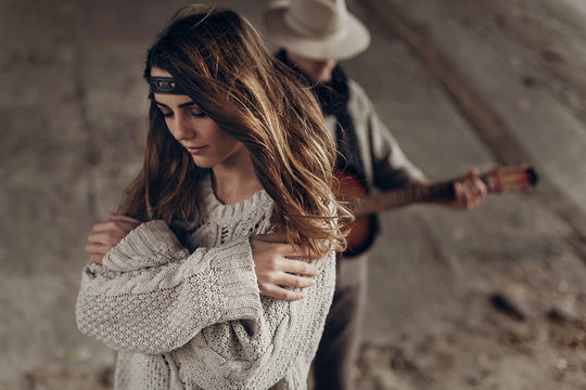 Beautiful sensual indie girl in hipster boho clothes posing in front of handsome cowboy guitar player outdoors