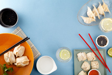 Asian dumplings with sauces and drinks on blue background. Top view with copyspace