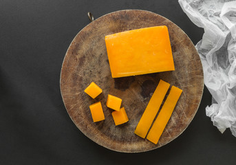 Block, slices and cubes cheddar cheese on cutting board