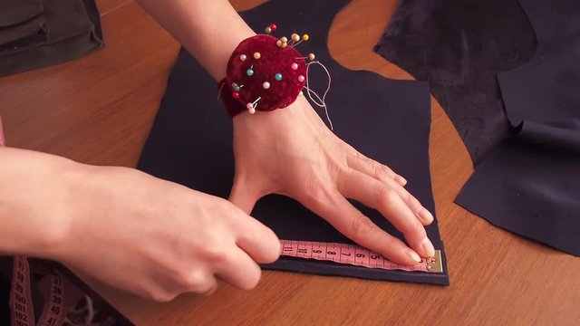 The seamstress measures with a centimeter tape. Close-up hands measure the product.