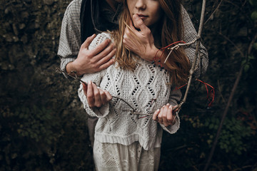 stylish hipster couple tender hugging. boho gypsy woman holding branch and man in hat embracing...