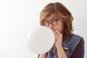 Girl inflates a balloon getting ready for a party. She's afraid of the explosion, so screwed up eyes