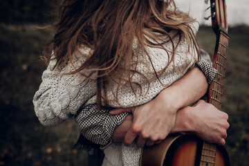 man with guitar hugging his boho gypsy woman closeup in windy field. atmospheric sensual moment....
