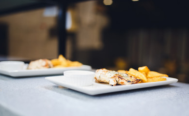 chicken breast cooked on the grill rests on a white plate, served with sauce and French fries slices in a rustic manner
