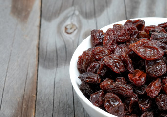 Dried grapes in white cup on wooden floor.