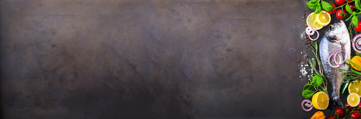 Fresh uncooked fish, dorado, sea bream with lemon, herbs, vegetables and spices on stone background. Top view. Banner