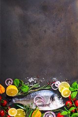Fototapeta na wymiar Fresh uncooked fish, dorado, sea bream with lemon, herbs, vegetables and spices on stone background. Top view. Banner