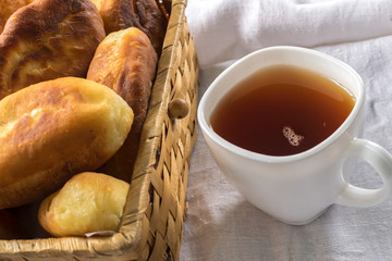 Traditional Homemade Baked Patties or Pies with Jam in a Wicker Basket next to a White Cup of Tea