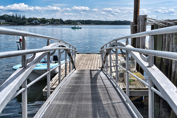 Handrails leading down to a floating dock with a lobster boat in distance at Searsport, Maine in the summertime.