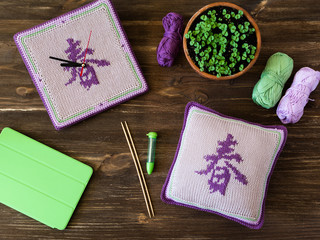 Knitted handmade watches,  square pillow, needles and lilac, green, white yarn balls on wooden table.  Translation of the hieroglyph is SPRING.