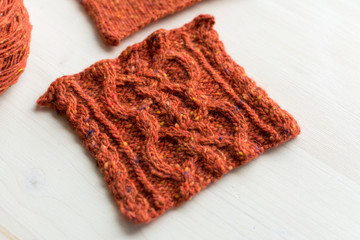 Knitted reddish-brown  square carpe and yarn ball on wooden table. Unfinished needlework in process.