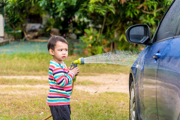Asian boy washing blue car by green water sprayer
