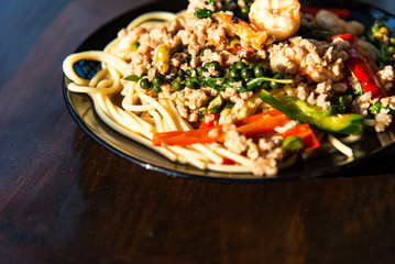 Drunken noodles seafood spaghetti in gray dish on wooden table.