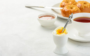 Delicious and healthy breakfast of boiled egg and brioche buns with black tea on a light background. Copy space,soft focus.