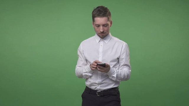 Young handsome man in white shirt standing and flipping his smartphone, chroma key green screen background