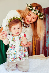 Stunning woman with golden hair holds her little daughter standing on soft bed