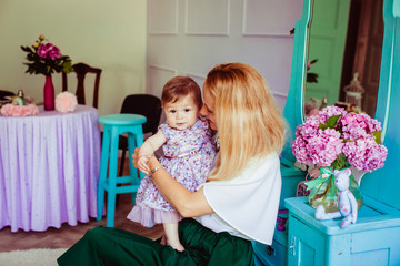 Blonde woman sits withher little daughter in dress with flowers