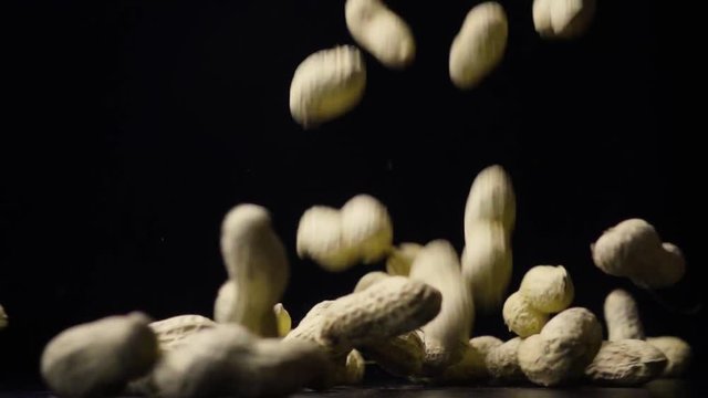 Unshelled peanuts in the shell falls on a table on black background slow mo