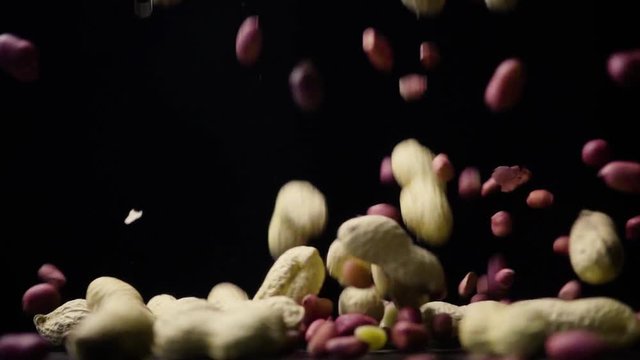Peanuts in shell and without shell falls on a table on black background slow motion