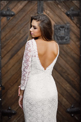 Obraz na płótnie Canvas Gorgeous charming sexy bride in white lace dress with bare backs against the background of old wooden doors
