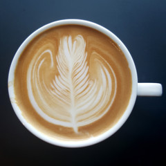 Top view of a mug of latte art coffee on black background.