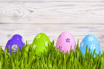 Pastel colored easter eggs in green grass over rustic wooden background.