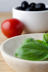 Basil Leaves, Tomato and Olives in Serving Bowls on Wood Planked Table