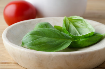 Fresh Basil Leaves in bowl with Tomato in Background