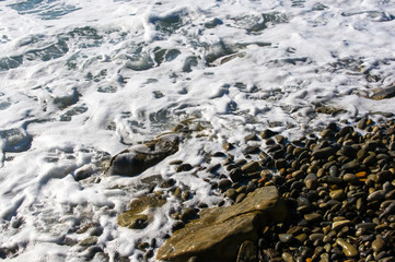 sea pebble beach with multicoloured stones, waves with foam