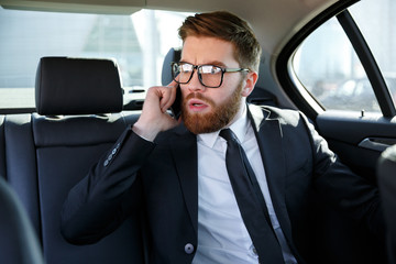 Frustrated business man in eyeglasses talking on mobile phone