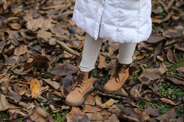Winter leather boots of a little girl on the dry autumn leaves